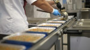 Porties voedsel in trays tijdens productieproces volgens HACCP systeem uitleg en gecontroleerde werkwijze
