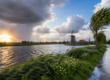 Nederlands landschap met wisselvallig weer, donkere regenwolken, zonneschijn, wind en een traditionele windmolen langs het water