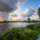 Nederlands landschap met wisselvallig weer, donkere regenwolken, zonneschijn, wind en een traditionele windmolen langs het water