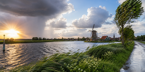 Nederlands landschap met wisselvallig weer, donkere regenwolken, zonneschijn, wind en een traditionele windmolen langs het water