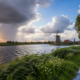 Nederlands landschap met wisselvallig weer, donkere regenwolken, zonneschijn, wind en een traditionele windmolen langs het water