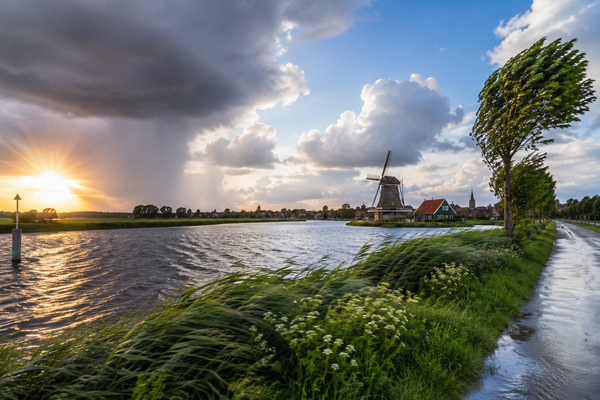 Nederlands landschap met wisselvallig weer, donkere regenwolken, zonneschijn, wind en een traditionele windmolen langs het water